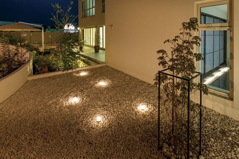 母屋の庭と離れのテラスを結ぶアプローチ脇には、白い石が敷き詰められ、アイアンで装飾された植栽が。地面に隠して設置されたライトが幻想的に照らします。
